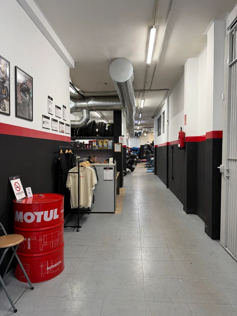 Entrada del taller MotoIntegra, con un bidón de Motul, camisetas del taller, el mostrador y el pasillo hacia la zona de trabajo